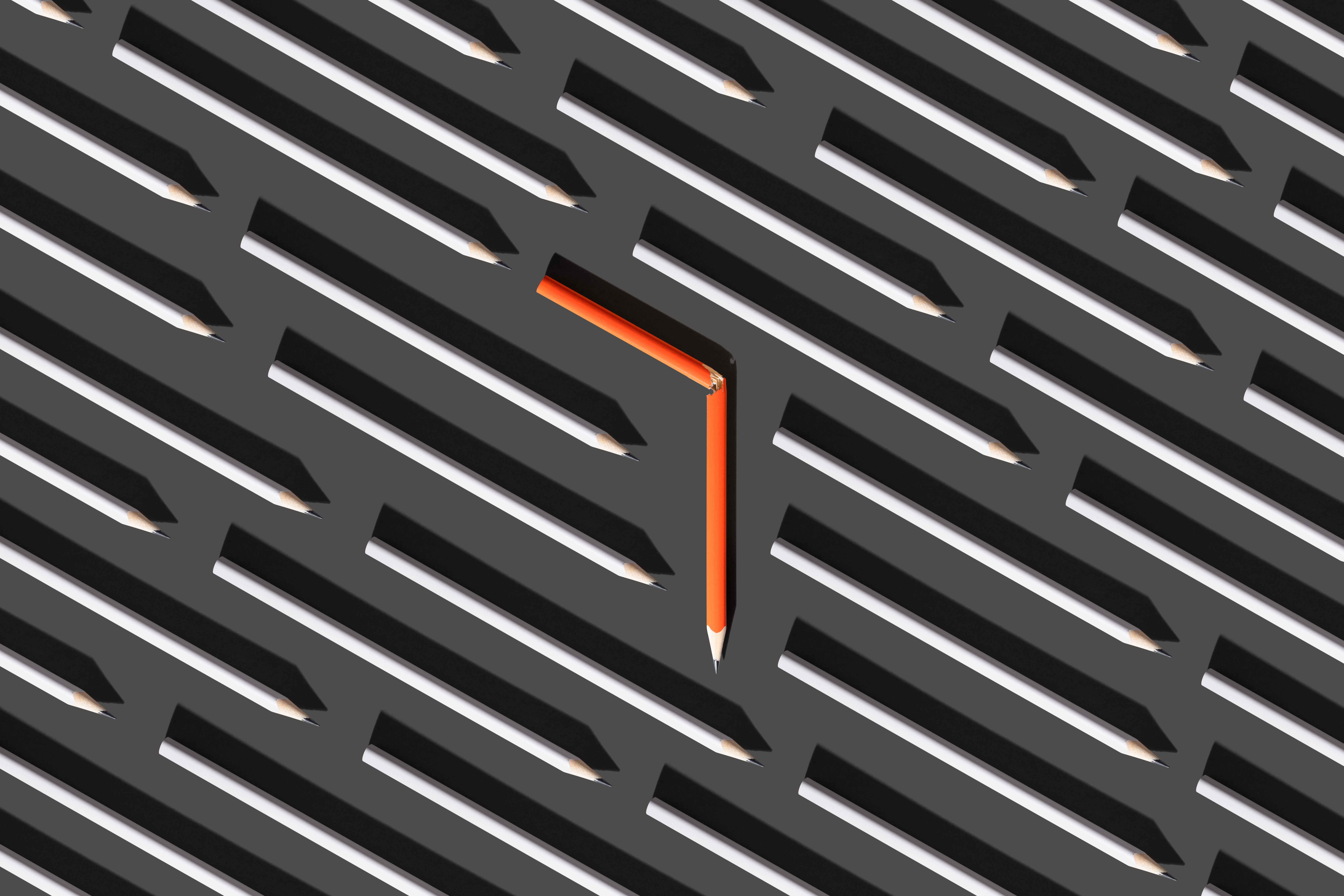 Dönmeyi temsil etmek için düz gri kalemler arasında turuncu kırık bir kalemin görüntüsü.