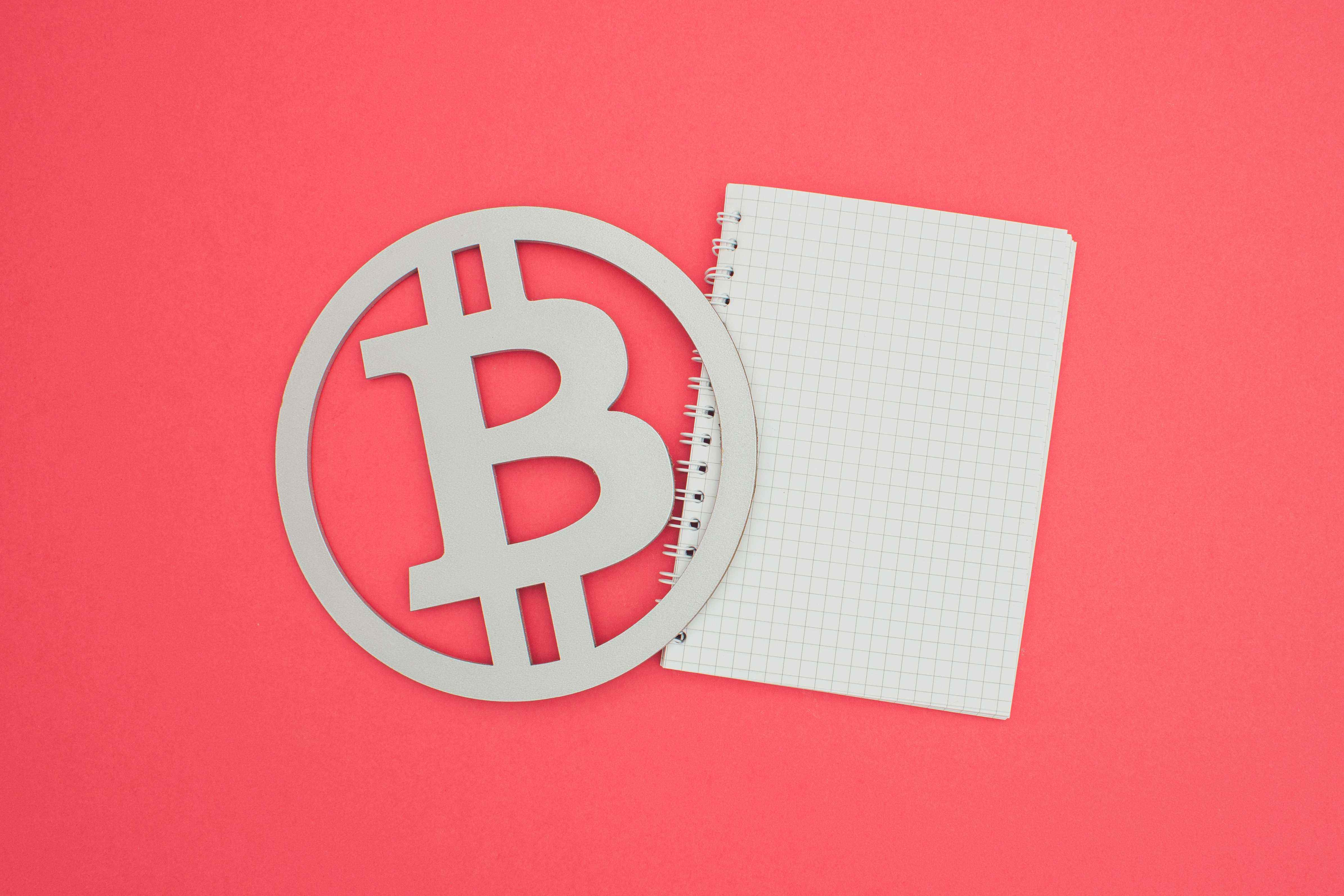 Bir Bitcoin sembolü ve somon arka planına karşı beyaz bir defter görüntüsü.