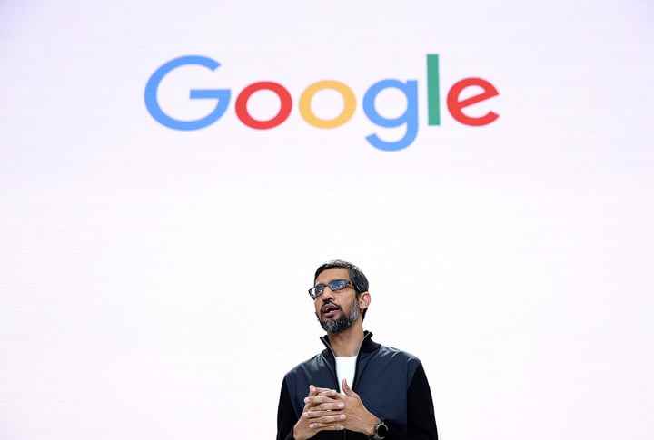 Google CEO'su Sundar Pichai, Google logosunu gösteren bir ekranın önünde duruyor.
