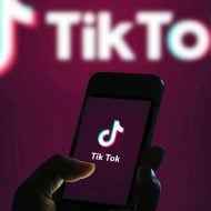 Bir kişinin cep telefonunu tuttuğu TikTok logosunun fotoğrafı.  996 çalışma yöntemi tartışmalıdır.