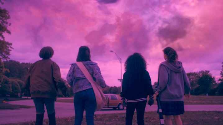 Sofia Rosinsky, Riley Lai Nelet, Camryn Jones ve Fina Strazza, Paper Girls'ten bir sahnede pembe bir gökyüzüne bakıyorlar.