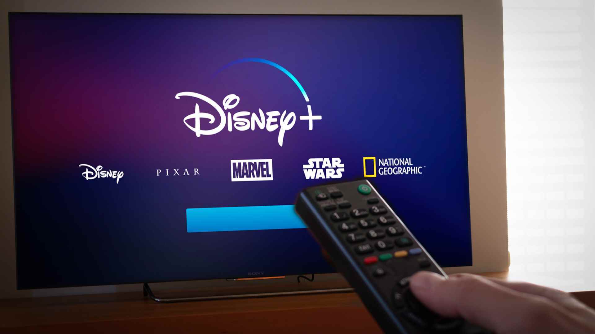 Disney Plus logosunu gösteren bir ekrana doğru uzaktan kumanda tutan bir adam