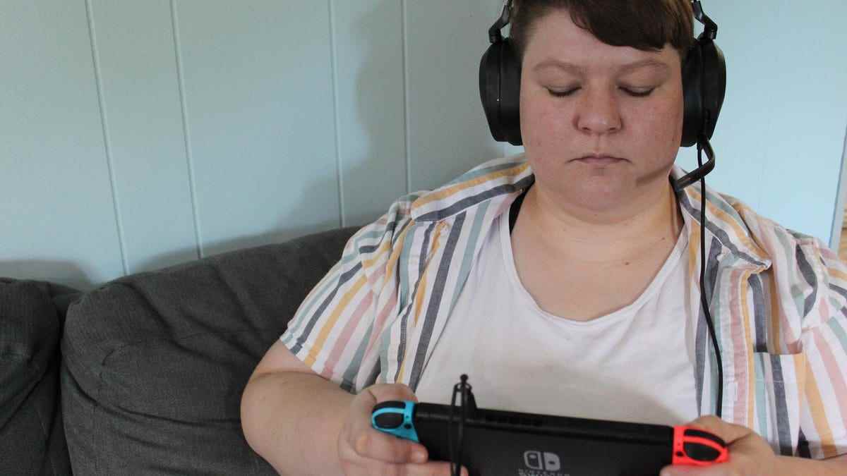 Taylor Clemons, Nintendo Switch'te oyun oynarken çok renkli çizgili bir gömlek ve Corsair HS65 Surround kulaklık takıyor