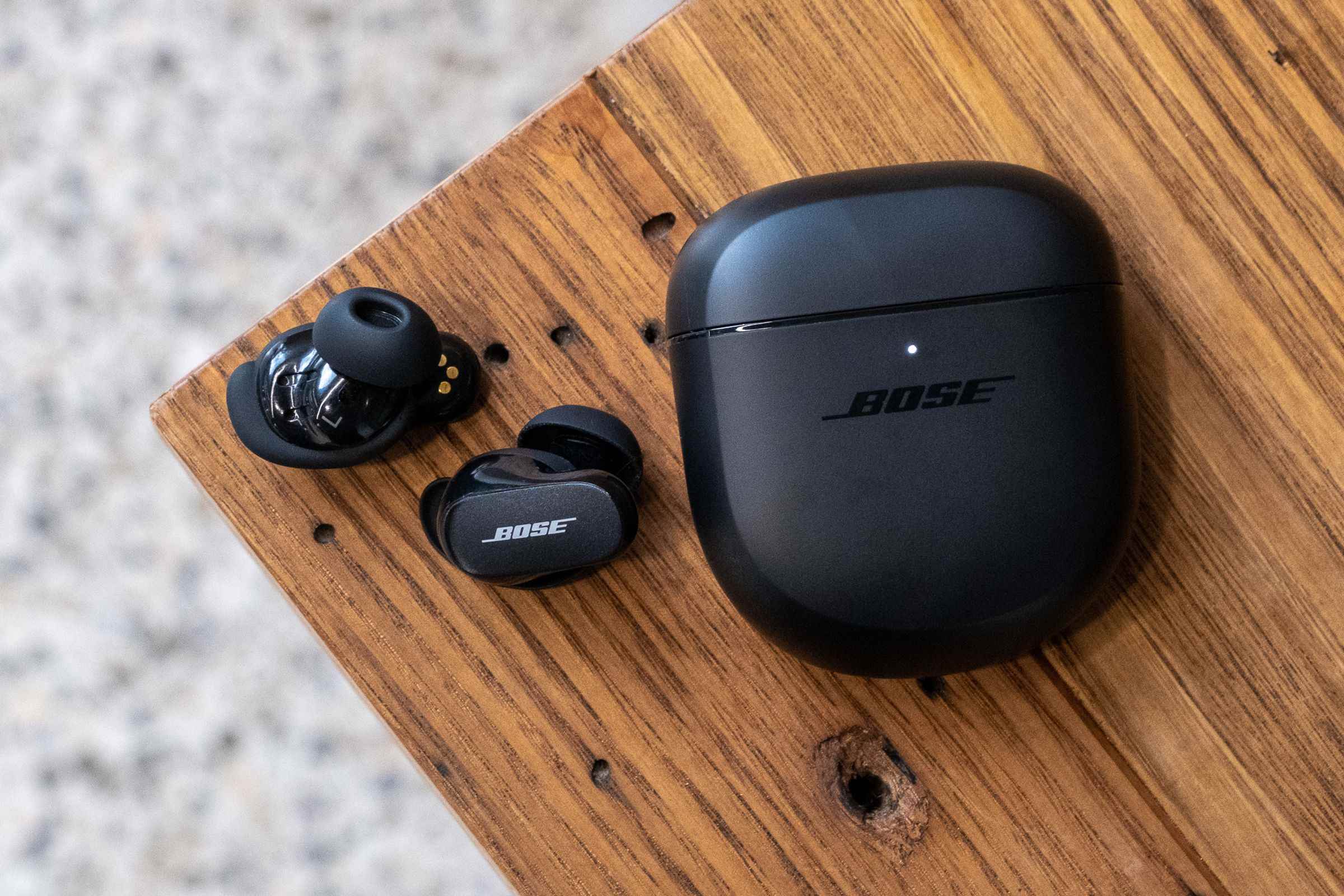 Ahşap bir masa üzerinde Bose QuietComfort Earbuds II'nin üstten bir görüntüsü.