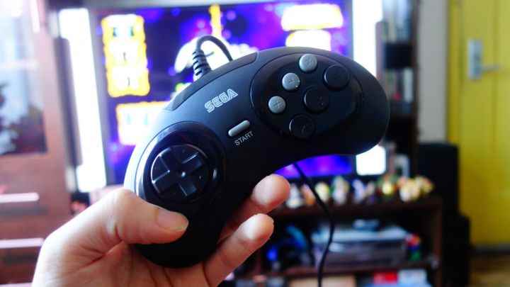 Bir TV'nin önünde tutulan bir Sega Genesis Mini denetleyicisi.