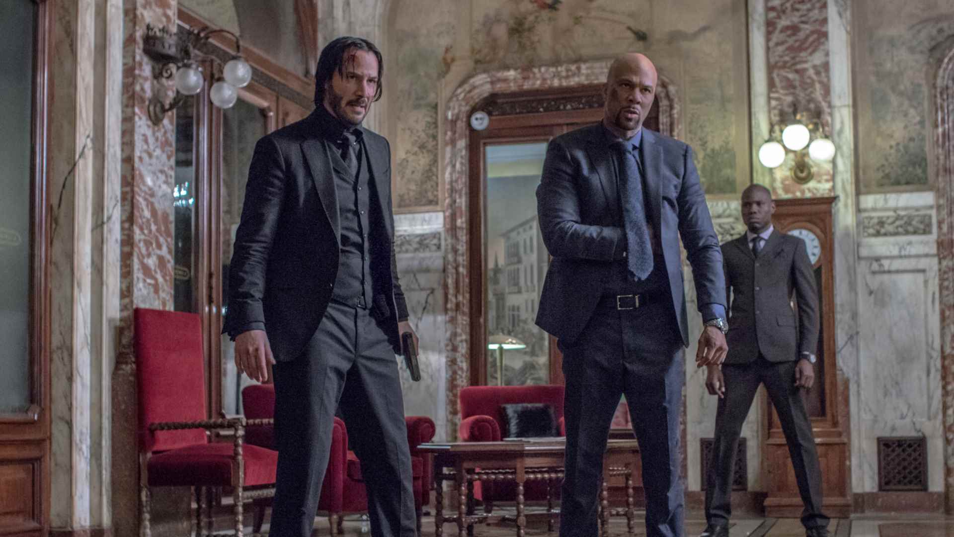 John Wick, John Wick'in filmlerinden birinde öfkeli görünen bir suikastçının yanında duruyor.