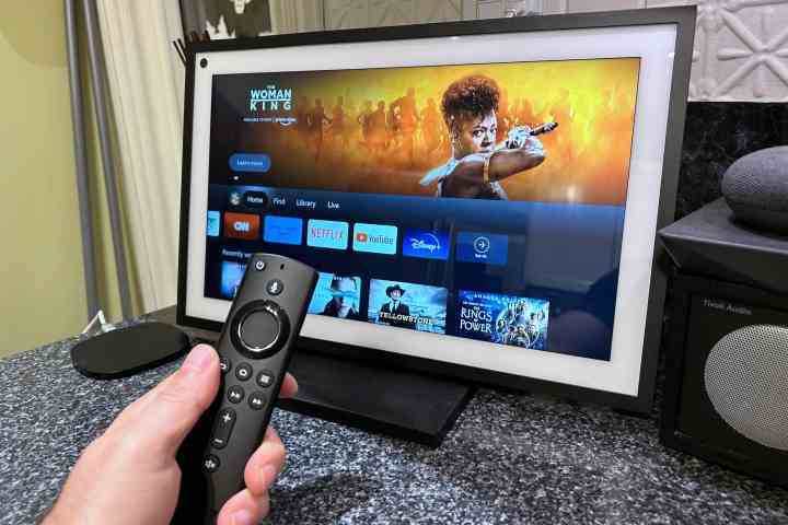 Ön planda bir Amazon Fire TV sesli uzaktan kumanda ile Fire TV deneyimini gösteren Amazon Echo Show 15.