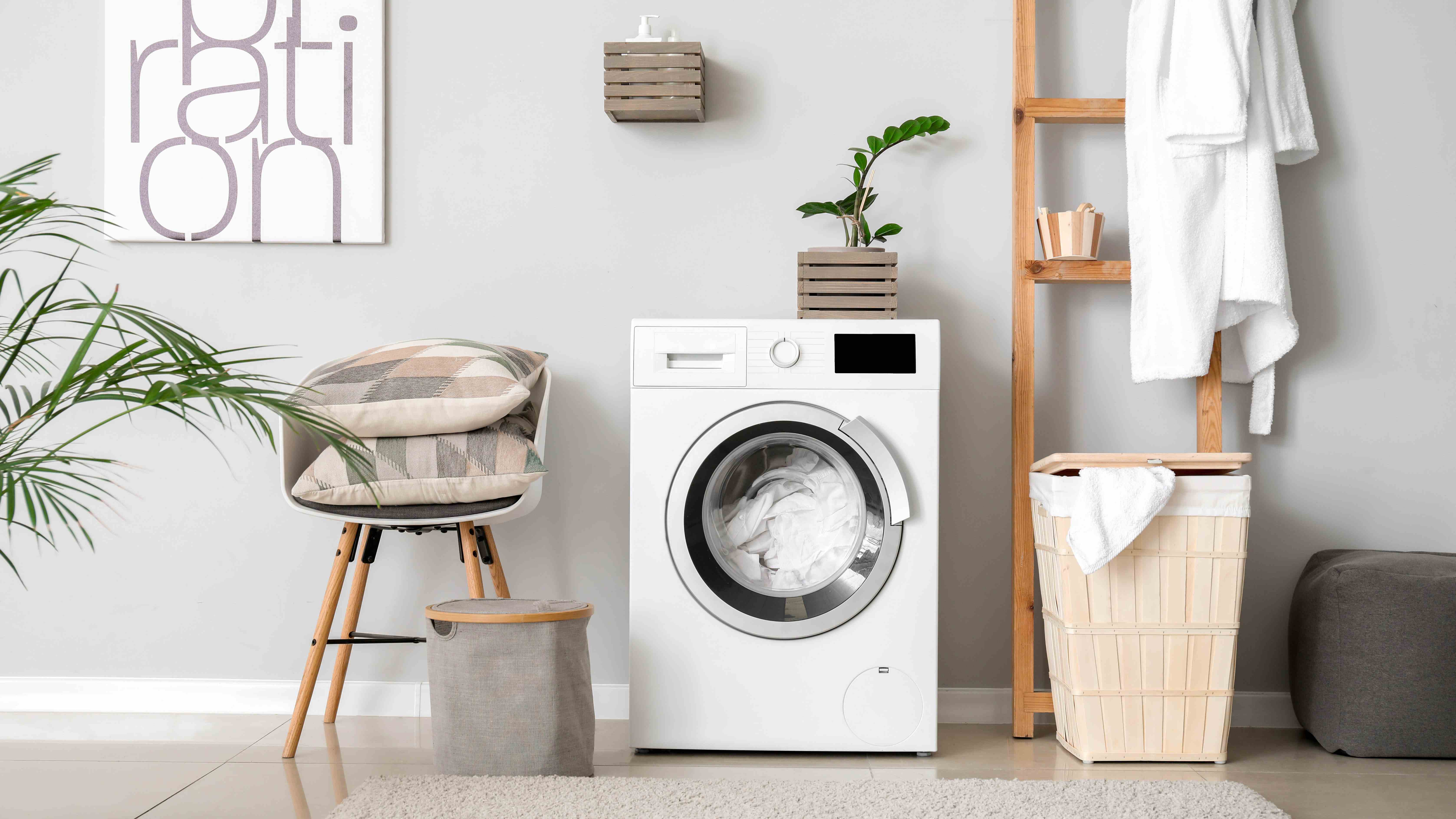 Çamaşır makinesi, çamaşır sepeti, sandalye, bitki ve raflar içeren bir çamaşır odası