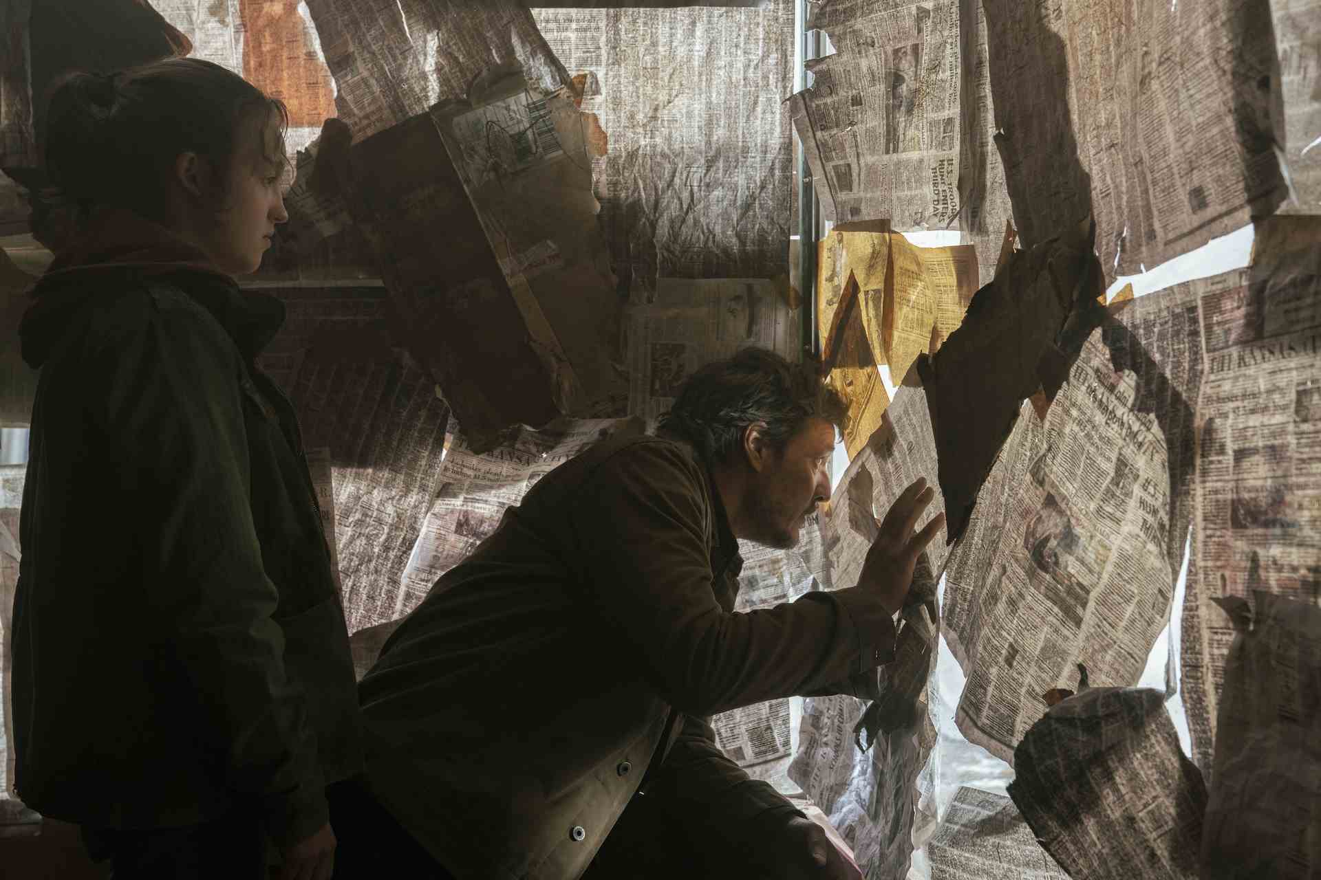 (Soldan Sağa) Bella Ramsey (Ellie olarak) ve Pedro Pascal (Joel olarak) HBO'nun The Last of Us 4. bölümünde gazetelerle kaplı bir barda saklanıyorlar.