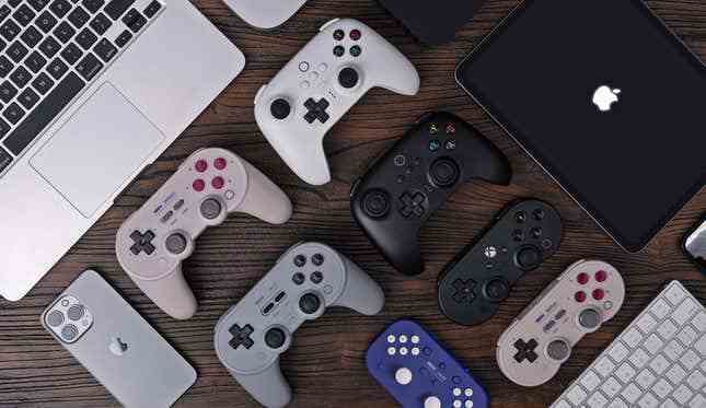 8BitDo kablosuz kontrol cihazları koleksiyonunun tamamı, artık Apple cihazlarıyla çevrili ahşap bir masa üzerinde oturan Apple cihazlarını destekliyor.