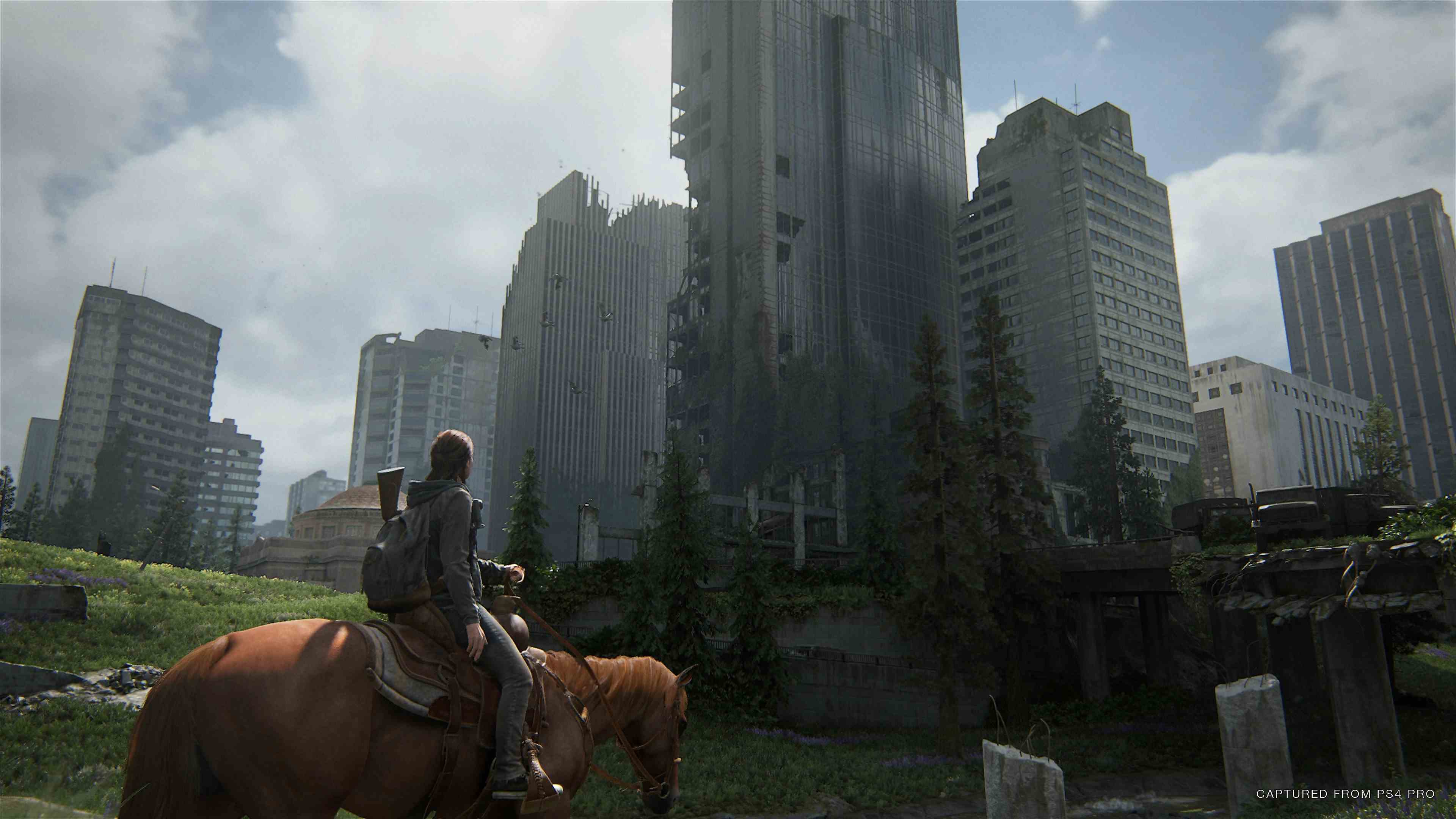 The Last of Us Part II'den bir ekran görüntüsünde bir şehir manzarasına yaklaşan bir at binicisi