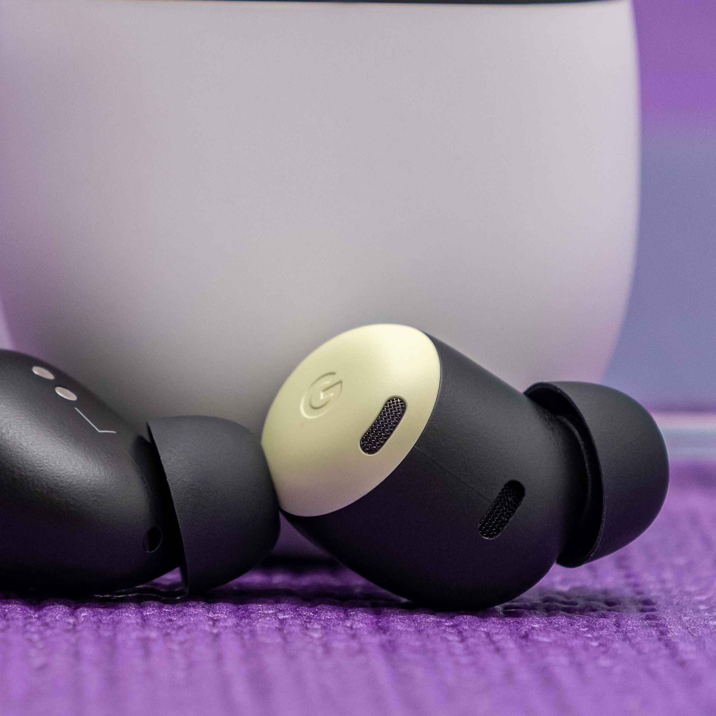 Google'ın sarı limon otu rengindeki Pixel Buds Pro kulakiçi kulaklıkları, bir masanın üzerindeki beyaz şarj kutusunun dibinde duruyor.