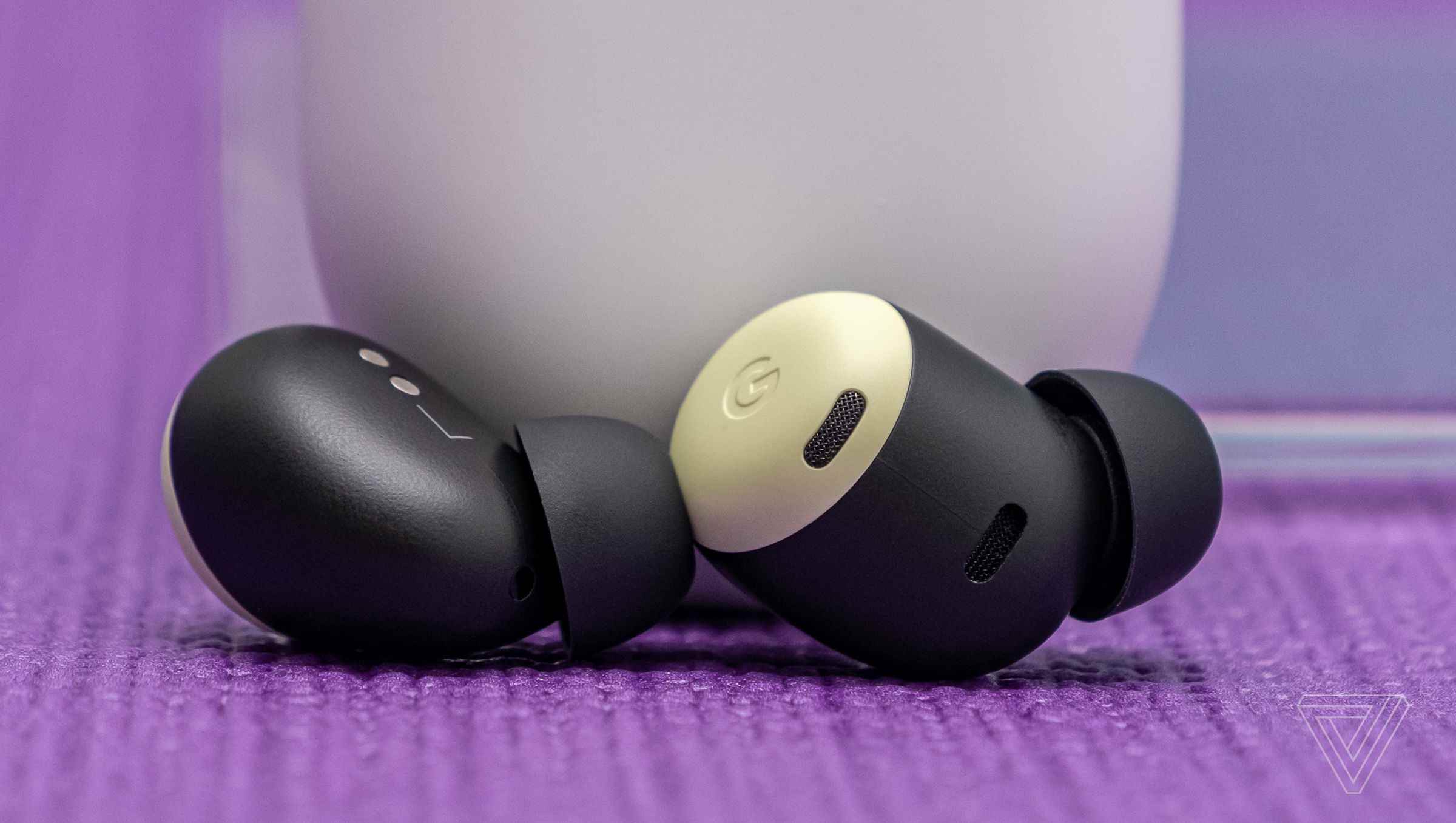 Google'ın sarı limon otu rengindeki Pixel Buds Pro kulakiçi kulaklıkları, bir masanın üzerindeki beyaz şarj kutusunun dibinde duruyor.