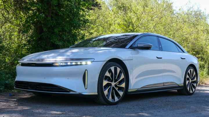 Yapraklı bir çitin önünde beyaz bir Lucid Air Ground Touring arabası. 