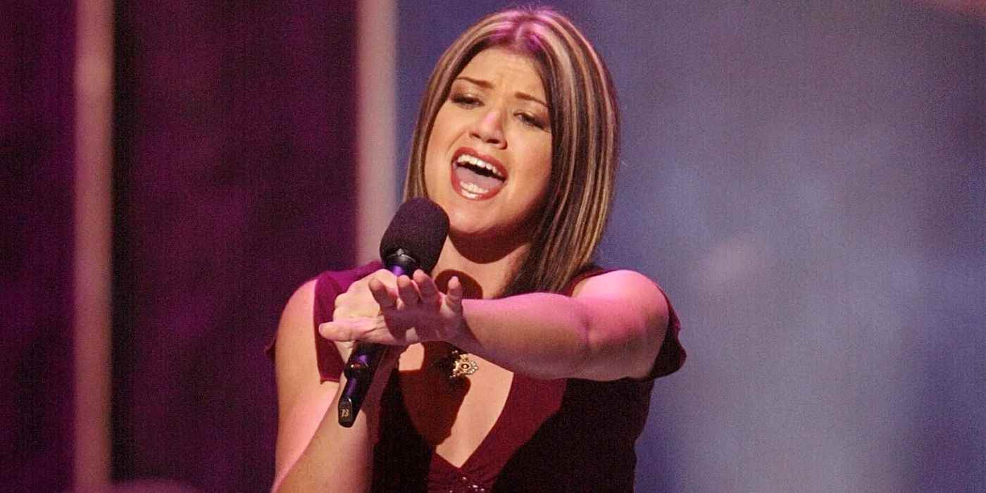 American Idol'da Kelly Clarkson elinde mikrofonla şarkı söylerken diğer elini uzatıyor