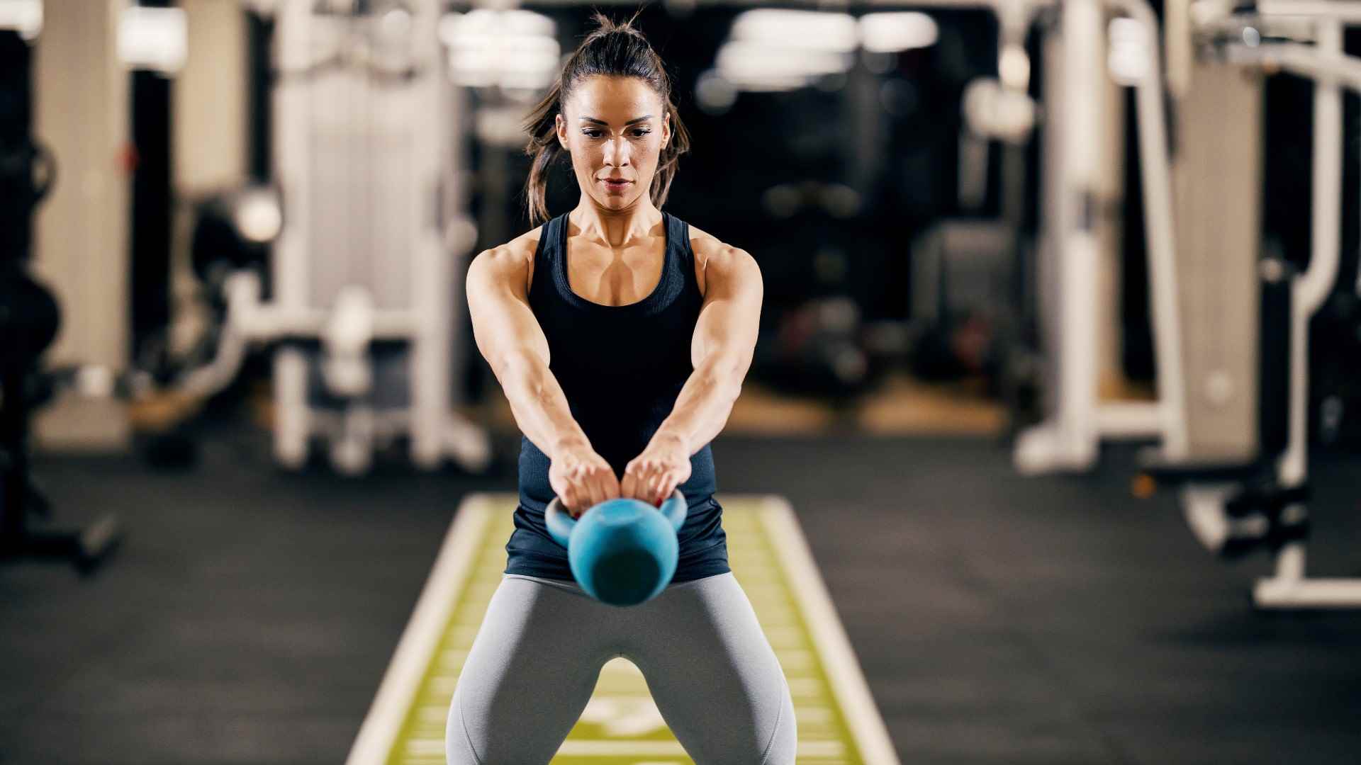 Ab egzersizi sırasında vücudunun önünde sallanırken iki eliyle önünde bir kettlebell tutan kadın