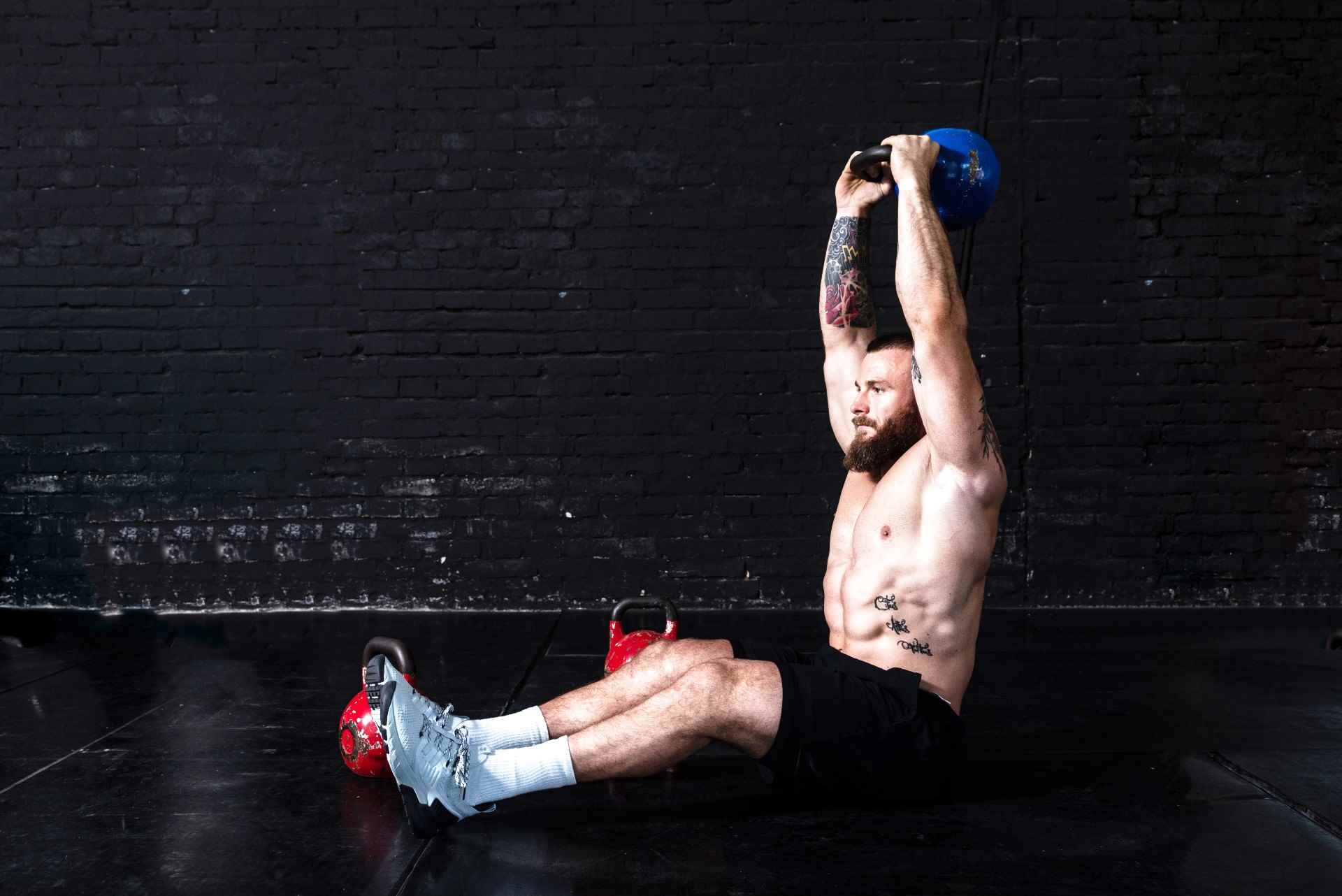 Kafasının üzerinde bir kettlebell tutarak mekik çeken adam