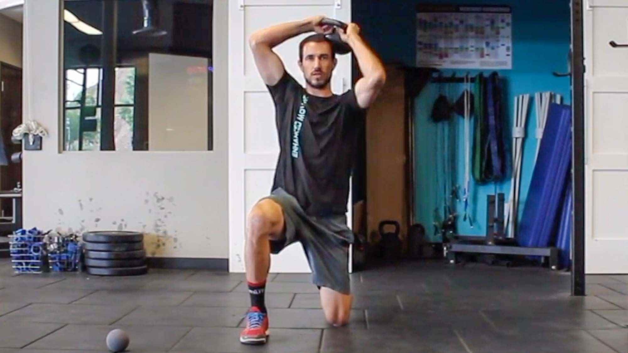 Spor salonunda yarı diz çökmüş kettlebell halo yapan adam