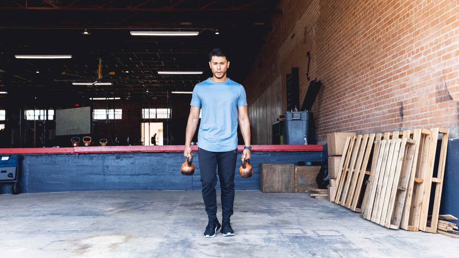 Her elinde birer tane tutan iki kettlebell ile bir çiftçi tutuşu gerçekleştiren adam