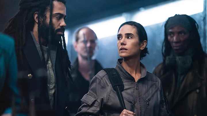 David Diggs ve Jennifer Connelly, Snowpiercer'dan bir sahnede arkalarında iki kişi olarak birbirlerine bakıyorlar.