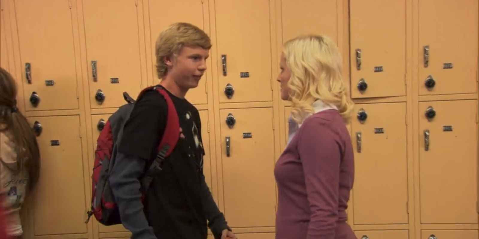 Leslie okul koridorunda Greg Pikitis ile konuşuyor.