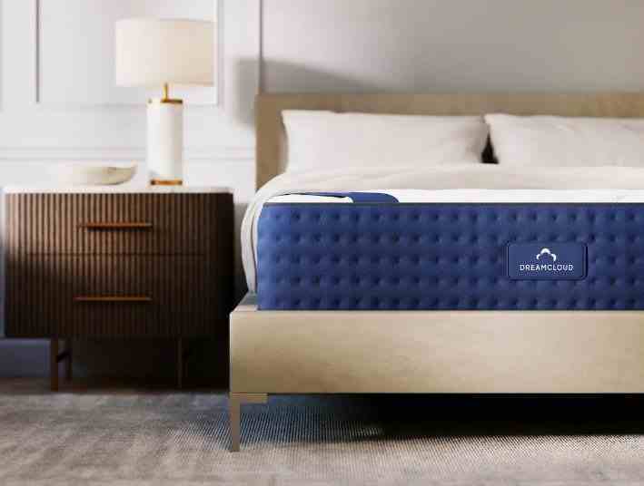Nötr bir yatak odasında ahşap yatak çerçevesi üzerinde DreamCloud hafızalı köpük şilte