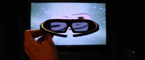 Televizyonun önünde bir dizi 3D gözlük tutan bir el.