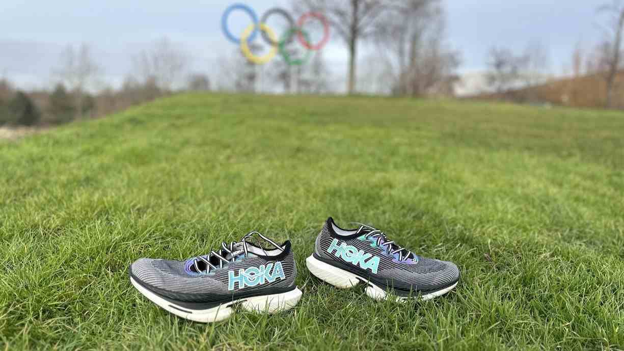 Hoka Cielo X1 Olimpiyat halkalarının önünde çim üzerinde koşu ayakkabısı