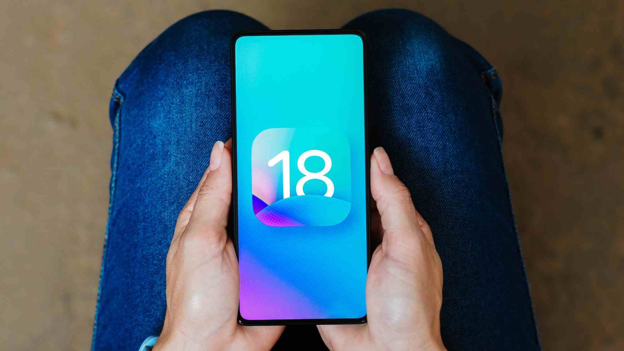 Bir kişinin kucağındaki iPhone'da iOS 18 logosu