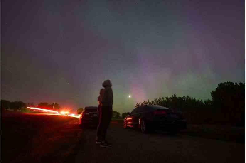 İnsanlar jeomanyetik fırtına sırasında Kuzey ışıklarını veya aurora borealis'i izlemek için Londra, Ontario yakınlarındaki bir köy yolunda duruyorlar